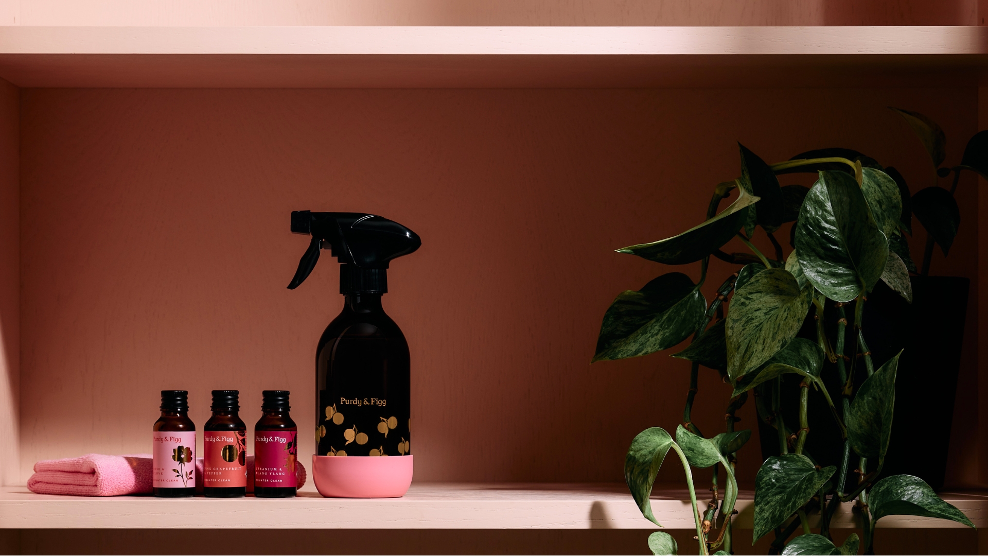 The spray, concentrates, base, and cloth in the Purdy &amp;amp; Figg x CoppaFeel! displayed in a pink room