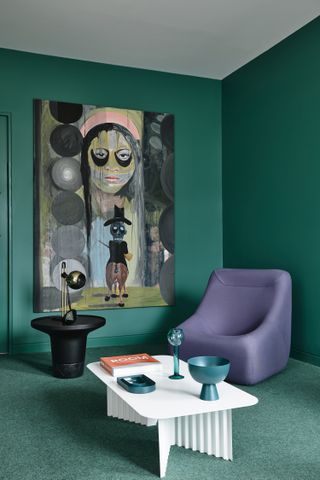 A living room with dark green walls and a purple armchair