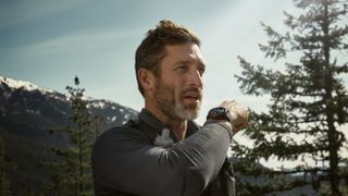 A photo of a man in the mountains wearing a Garmin Fenix 8 Pro, using it to call someone using LTE cellular data.