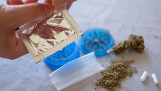 man opening small gold package over a table with spice (synthetic marijuana) and small plastic dishes on it