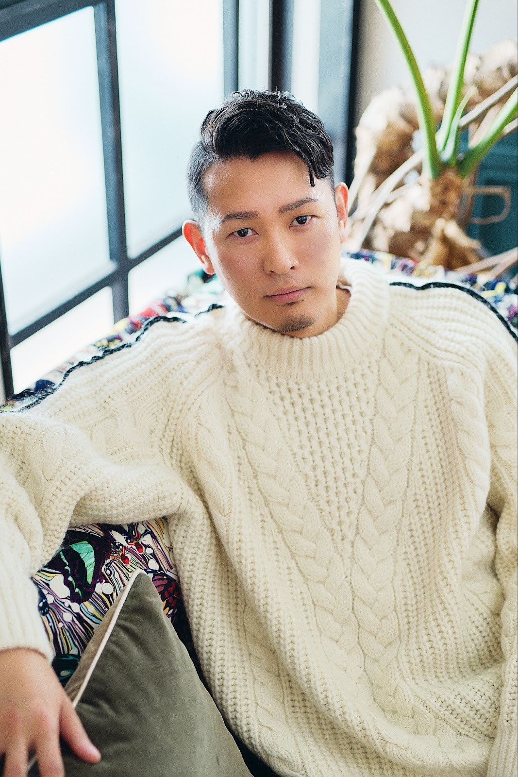 A Japanese man named Kazuyuki wears a white fisherman's sweater while posing on a printed sofa, in a cast portrait for 'The Boyfriend.'