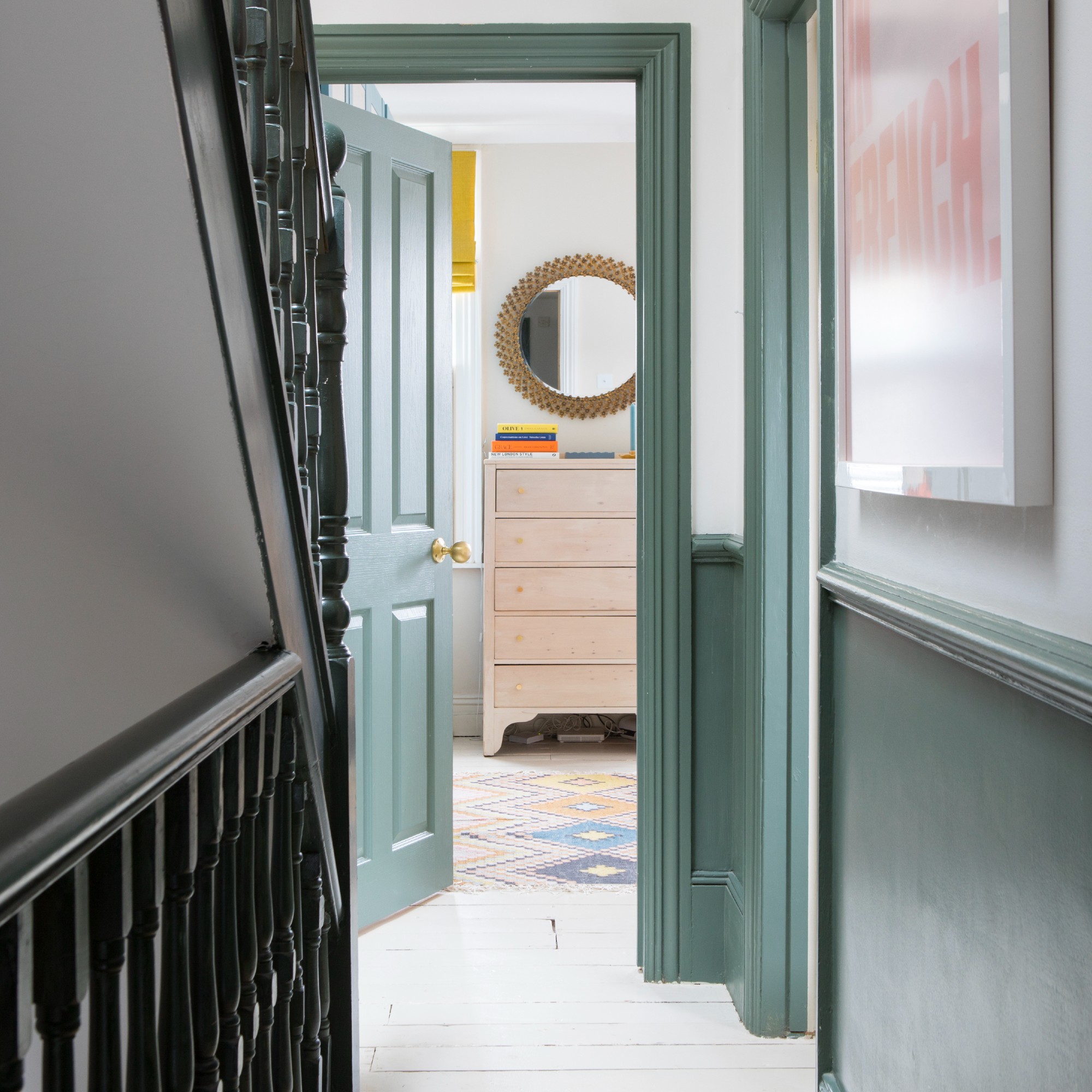 A narrow hallway with a dado rail on the walls, painted half dark green on the bottom and half white on the top 