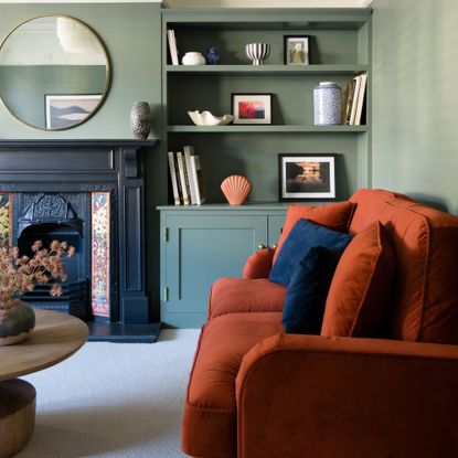 A living room with sage green walls, a rust red sofa and a light-coloured carpet