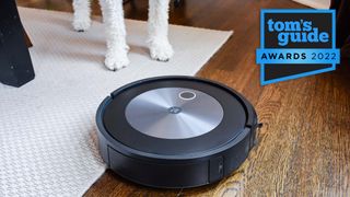 iRobot Roomba J7+ vacuuming a living room carpet with a dog nearby