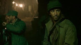 Three men in a cave, the man furthest to the right is Tom Morello in Iron Man.