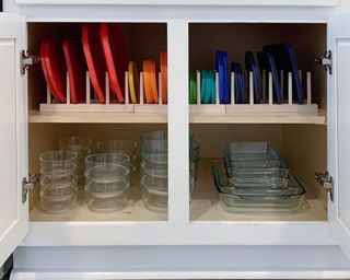 A cupboard with glass Tupperware and colored lids organized in color order in wooden rack