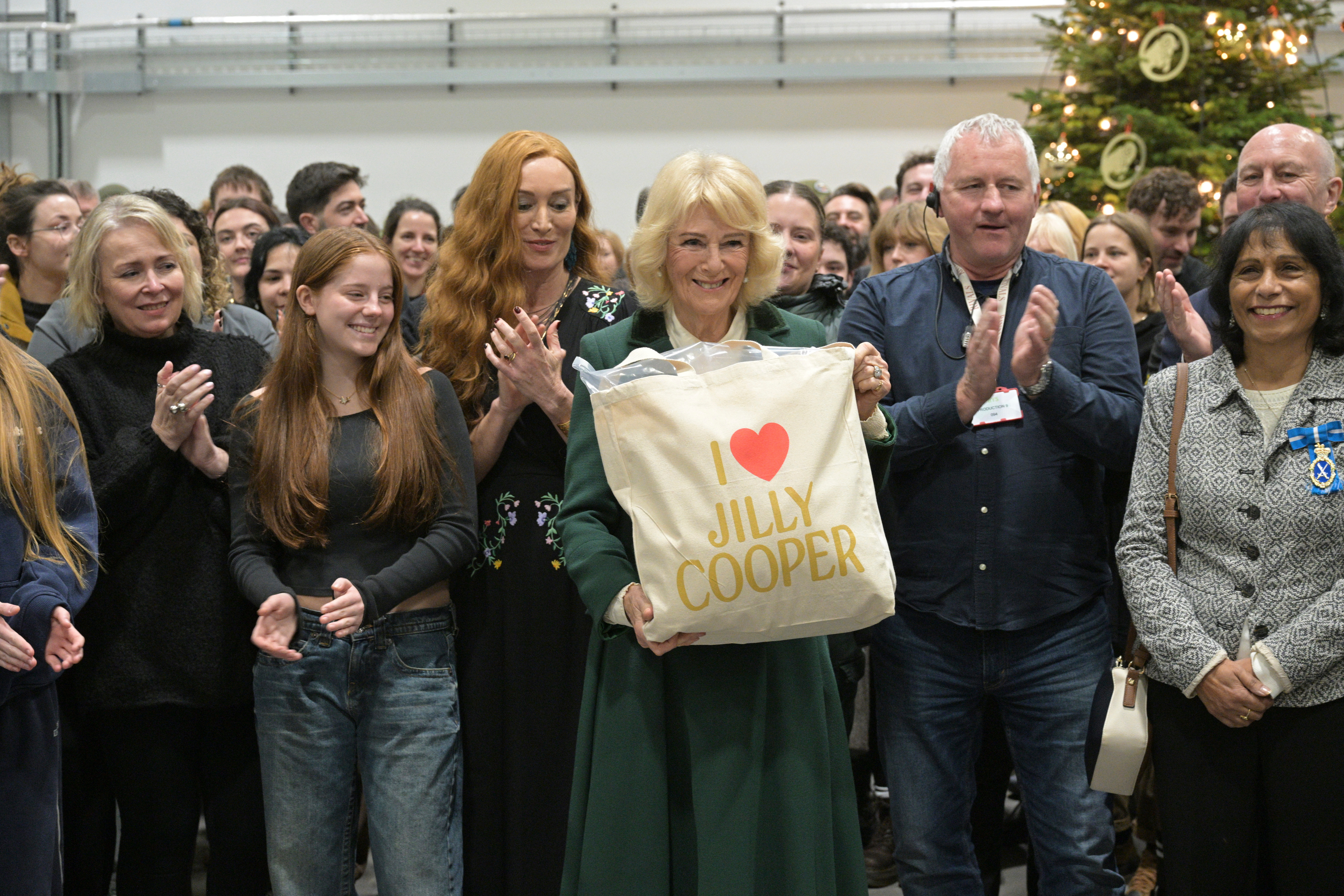 Queen Camilla holding an I heart Jilly Cooper tote bag with the cast of Rivals