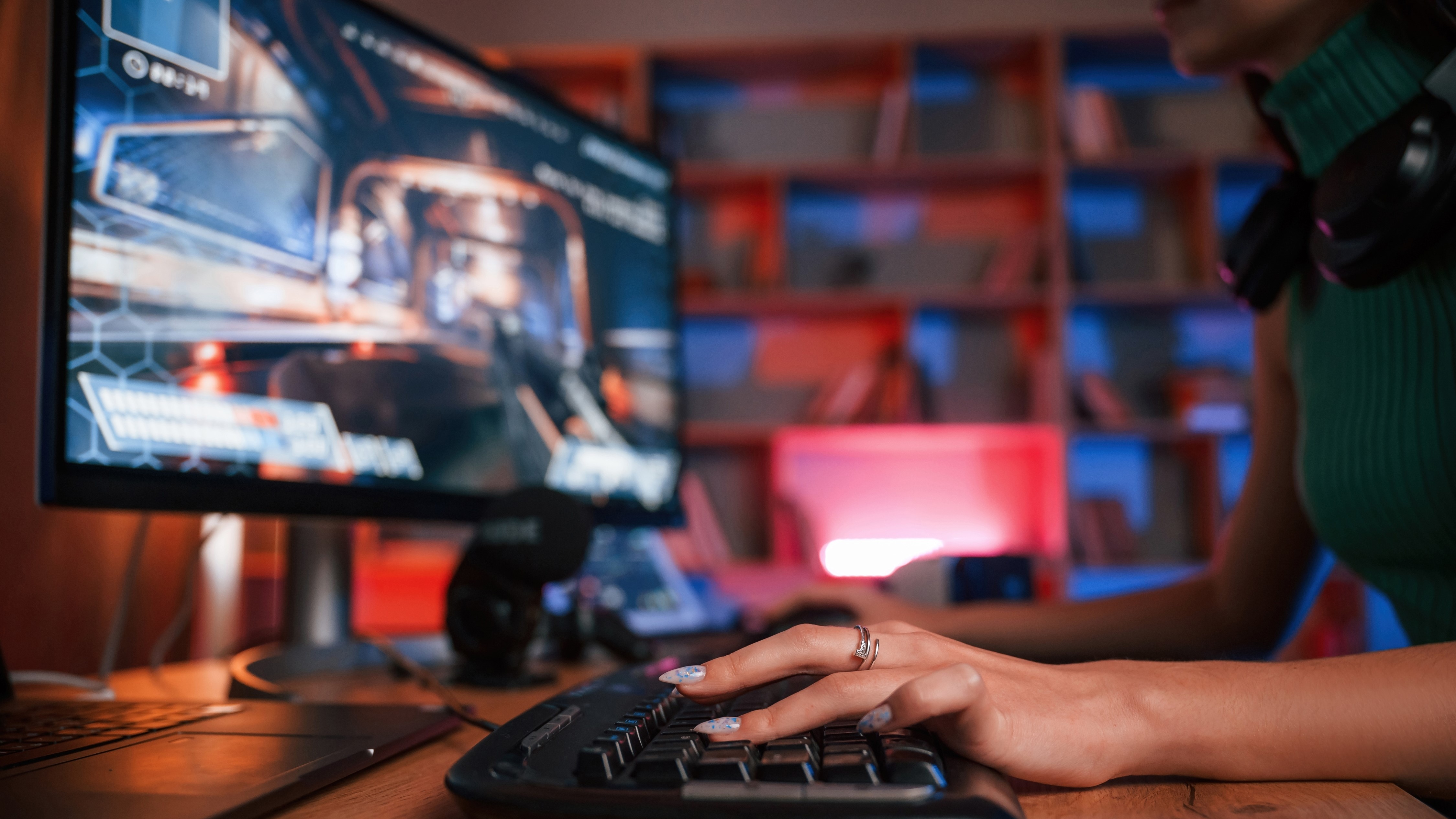 A close up of a keyboard and a woman gaming at a PC in neon lighting