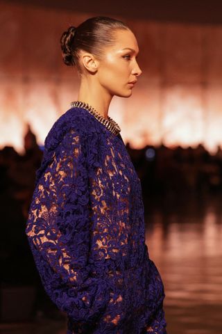 a side profile of Bella Hadid on the paris fashion week runway for saint laurent wearing a blue lace naked dress and a collar necklace