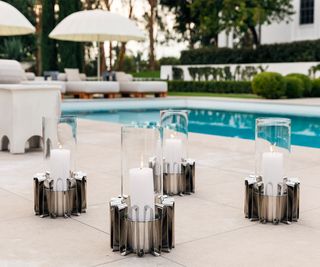 Four large candle holders on the decking by an outdoor swimming pool.
