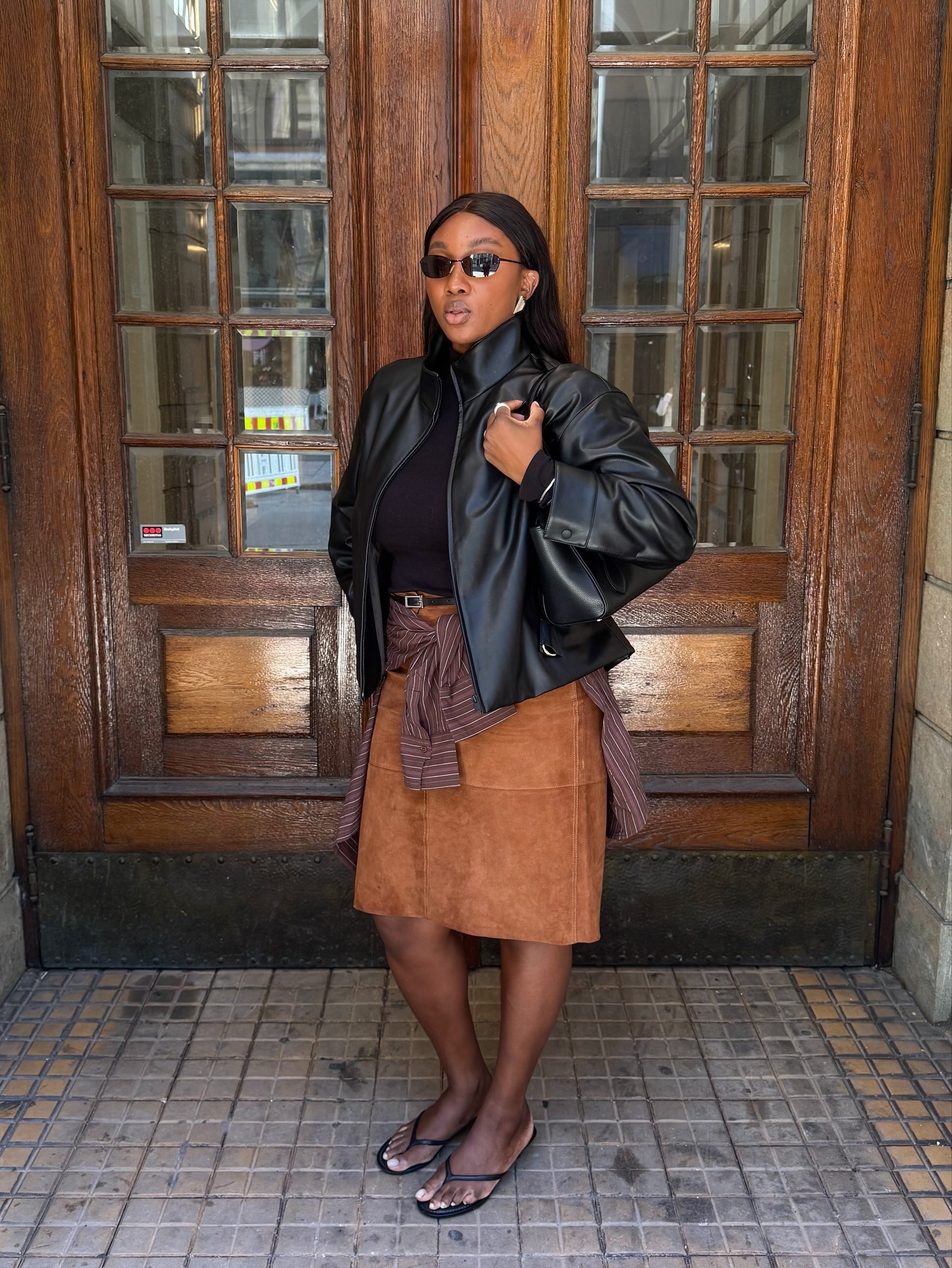 Influencer @nnennaechem wears a brown suede skirt with a black leather jacket and black flip-flops.