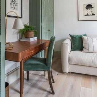 A living room with a cream sofa, light wood flooring and a desk with a green velvet chair