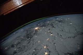 A lime-green aurora glows above Earth's city lights in this view from the International Space Station. At the time this photo was taken, the space station was orbiting about 258 miles (415 kilometers) above Russia and the Ukraine. A portion of the space station's solar array is visible in the top left corner of the image.