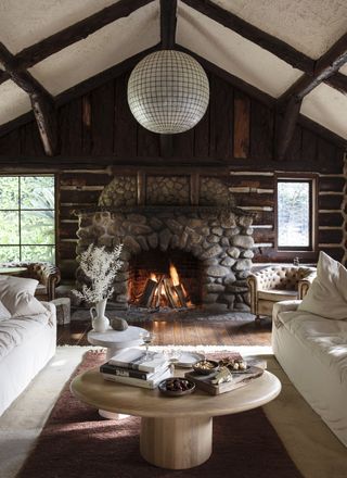 A cabin-style living room with a stone fireplace, wooden ceiling and a round wooden coffee table