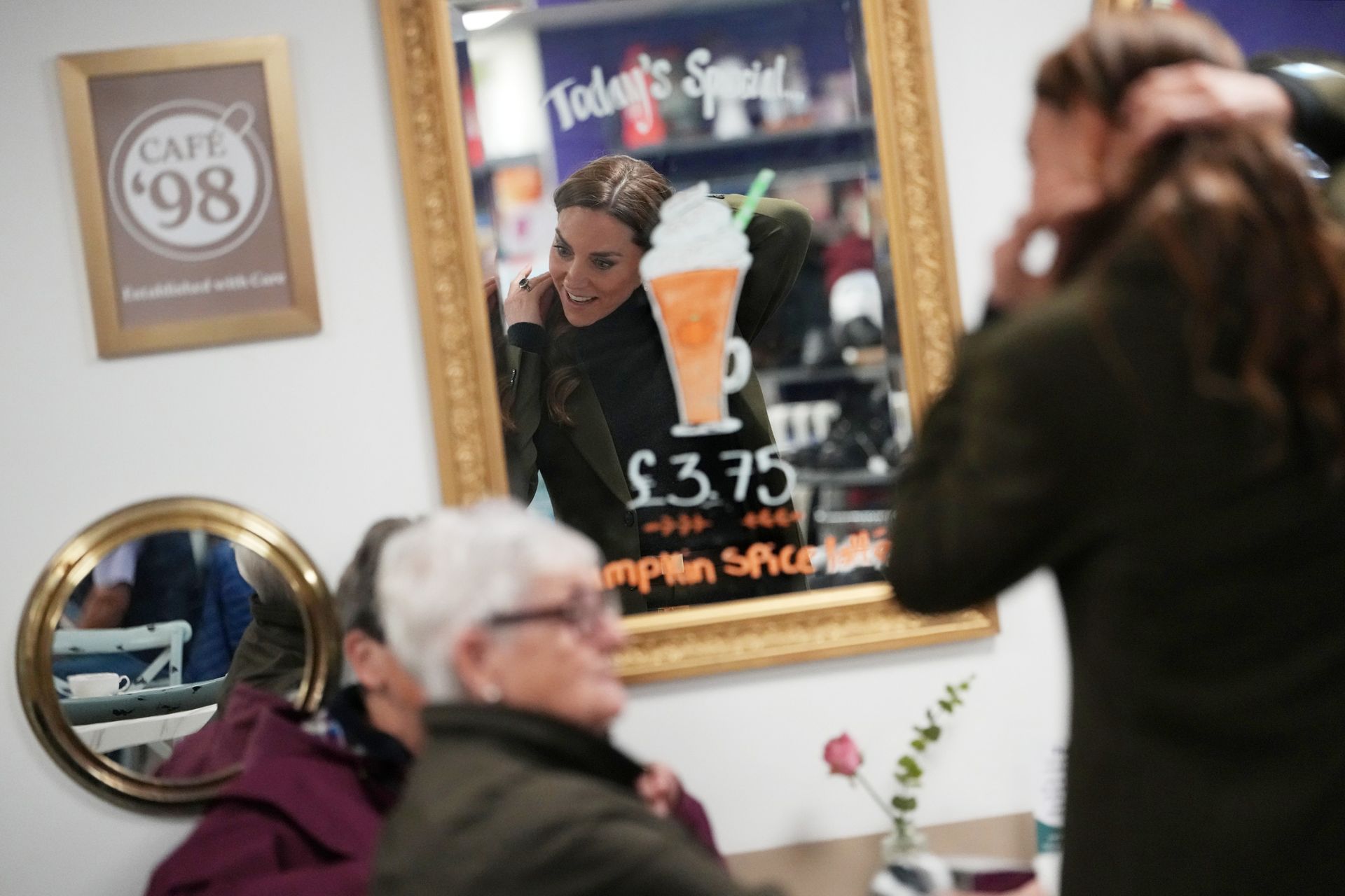 Princess Kate pulling her hair back and talking to two women at a cafe