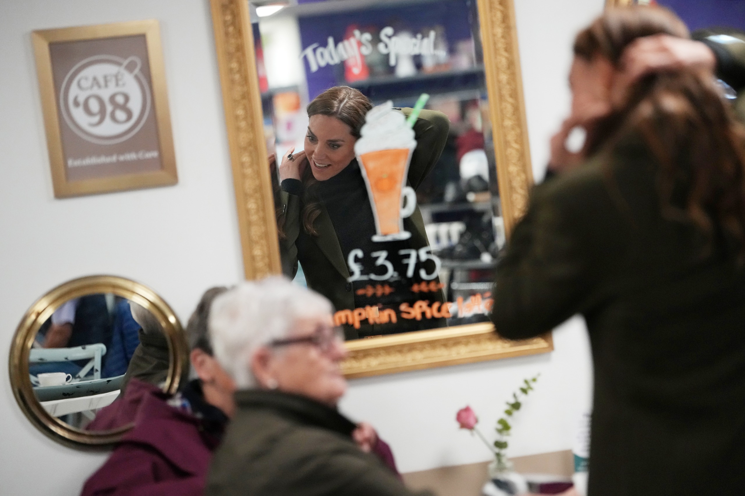 Princess Kate pulling her hair back and talking to two women at a cafe