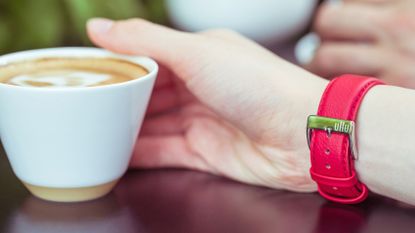 A hand reaching for a coffee, showing one of the best Apple Watch bands from Ullu