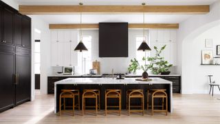 White and black kitchen with high cabinets, houseplants on the counters and a large central island with bar chairs