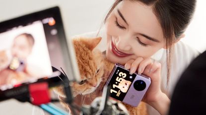 The Vivo X Flip in purple, being held by actress Wang Ziwen, who is also holding a ginger cat.