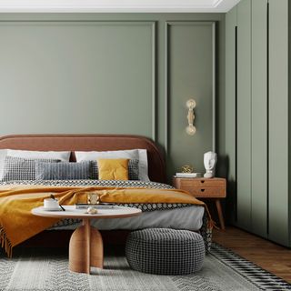 small bedroom colour ideas, green bedroom with green panelled walls, leather bed with monochromatic bedding, pouffe and rug. wooden side table and coffee table, saffron throw and cushion, wooden floors