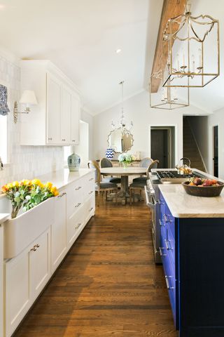 Galley kitchen with white units facing blue units and stove with pendant lights and dining area beyond
