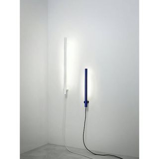 Two wall lamps, one white and one black, shaped like essential tubes and with black cables coming out the bottom