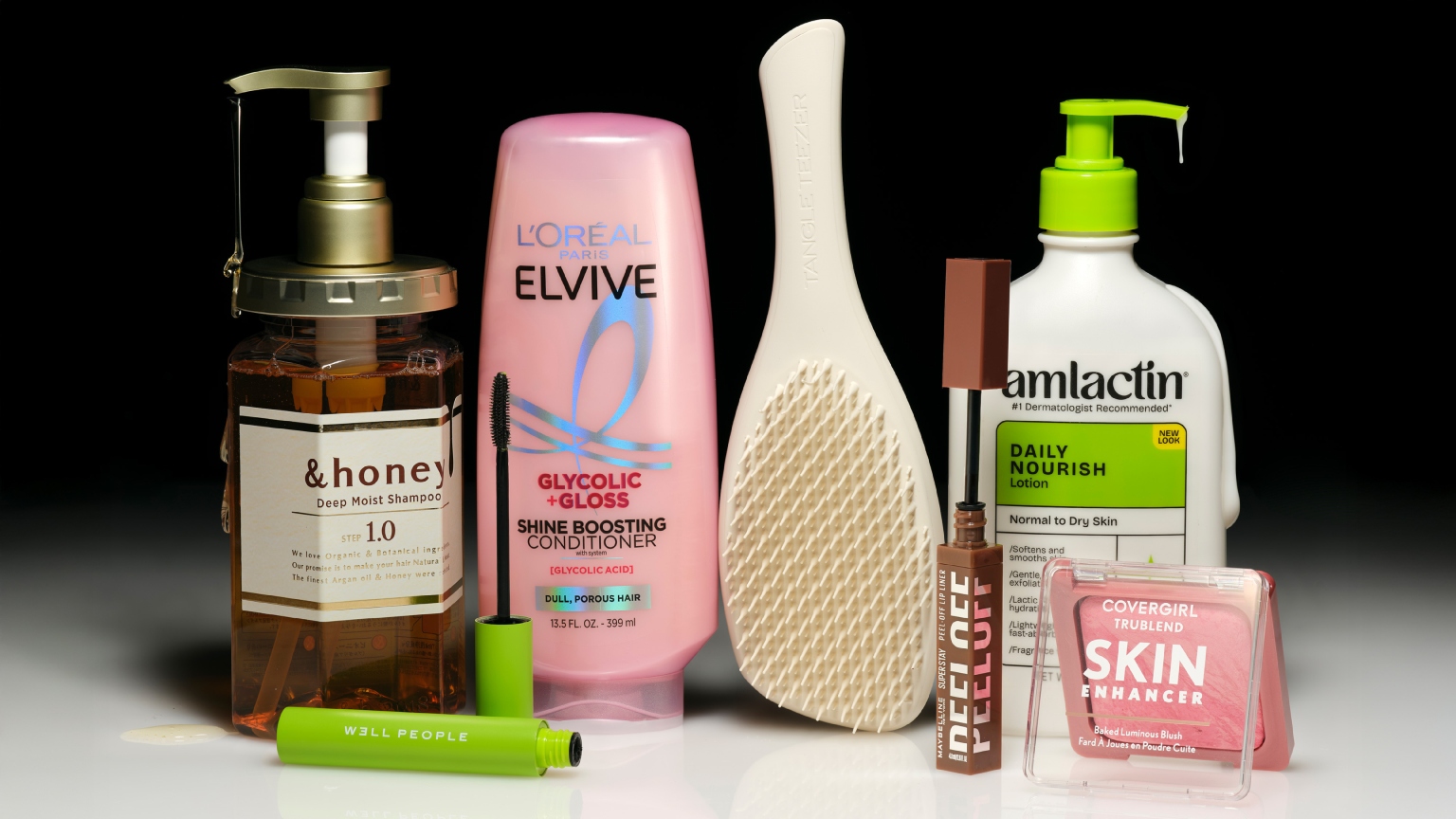 an array of drugstore beauty products on a white ground with a black background