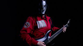 Mick Thomson of Slipknot wears a mask and a red boiler suit as he plays his ESP signature model in this portrait against a black background.