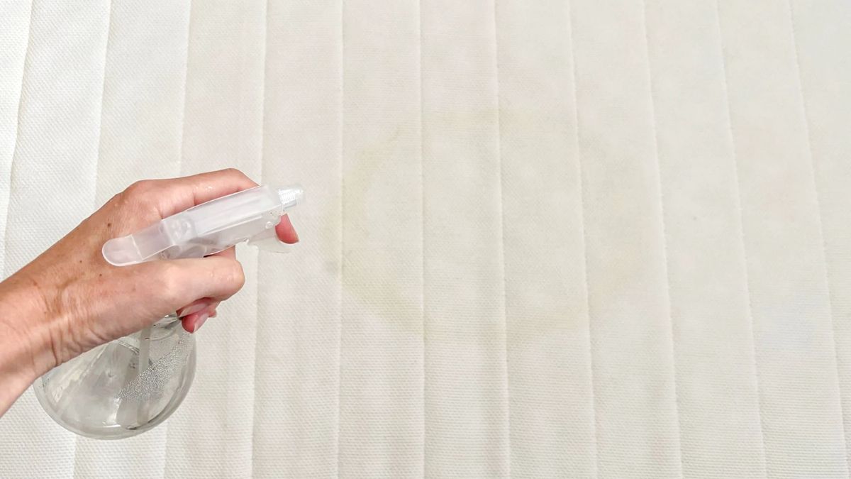 A woman sprays a cleaning solution onto a yellow mattress stain.