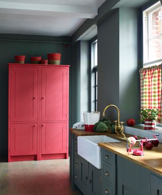 A dark gray kitchen color scheme with coral red painted pantry and gingham blinds.