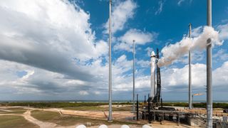 rocket on the launch pad with partly cloudy sky above.