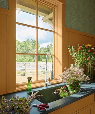 A green wallpapered kitchen with yellow painted window over a sink and yellow back splash panelling