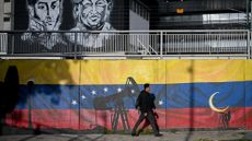 Man walking in front of a Venezuela flag with oil machinery on it