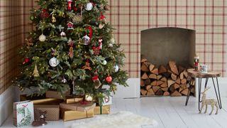 Living room with tartan check wallpaper on wall with log pile in empty fireplace with Christmas tree