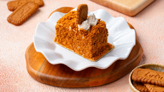 A biscoff flavoured cake placed on a plate that is surrounded by biscoff biscuits