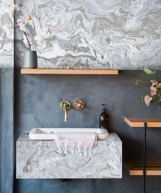Wall mounted marble sink with floating shelf above and brass wall mounted taps