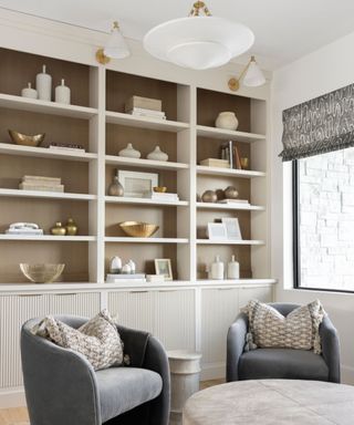 A room with white built-in bookshelves, two dark gray armchairs, and a light gray ottoman