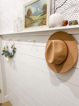 DIY accent wall with shiplap and wallpaper plus hat hanging off white pegs