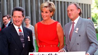 Princess Diana in a red scoop neck dress stood between two men in suits as they present her with a check thats being donated to Northwick Park Hospital