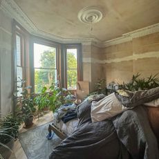 bedroom mid renovation with bare plaster walls and pillows piled on the bed