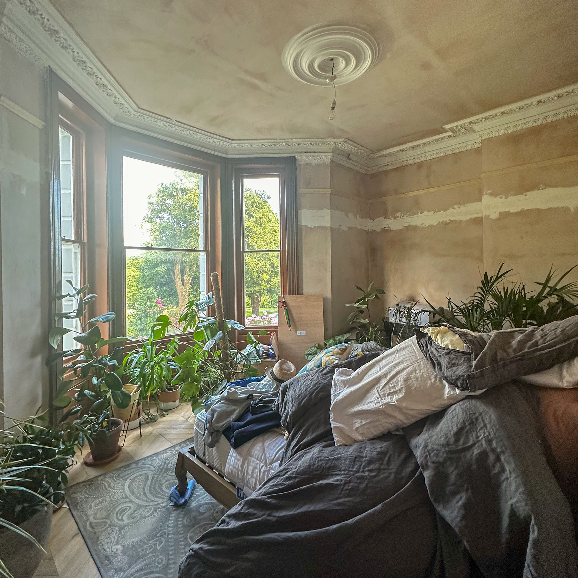 bedroom mid renovation with bare plaster walls and pillows piled on the bed