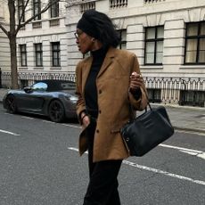 Influencer @georgia_3.0 wears a brown suede blazer with a black turtleneck, black trousers and black pointed-toe boots.