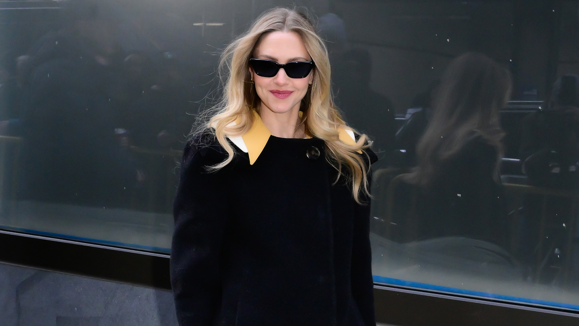 Amanda Seyfried wearing a black coat and sunglasses. 
