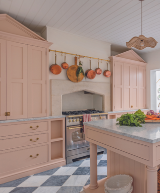 pink cabinets in kitchen with black and white checkerboard marble floor and grey marble top and copper saucepans hanging and rattan scallop pendant lamp