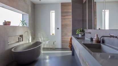 A modern industrial spa bathroom with grey bathtub, grey floor, mirrored wall and two recesses in wall