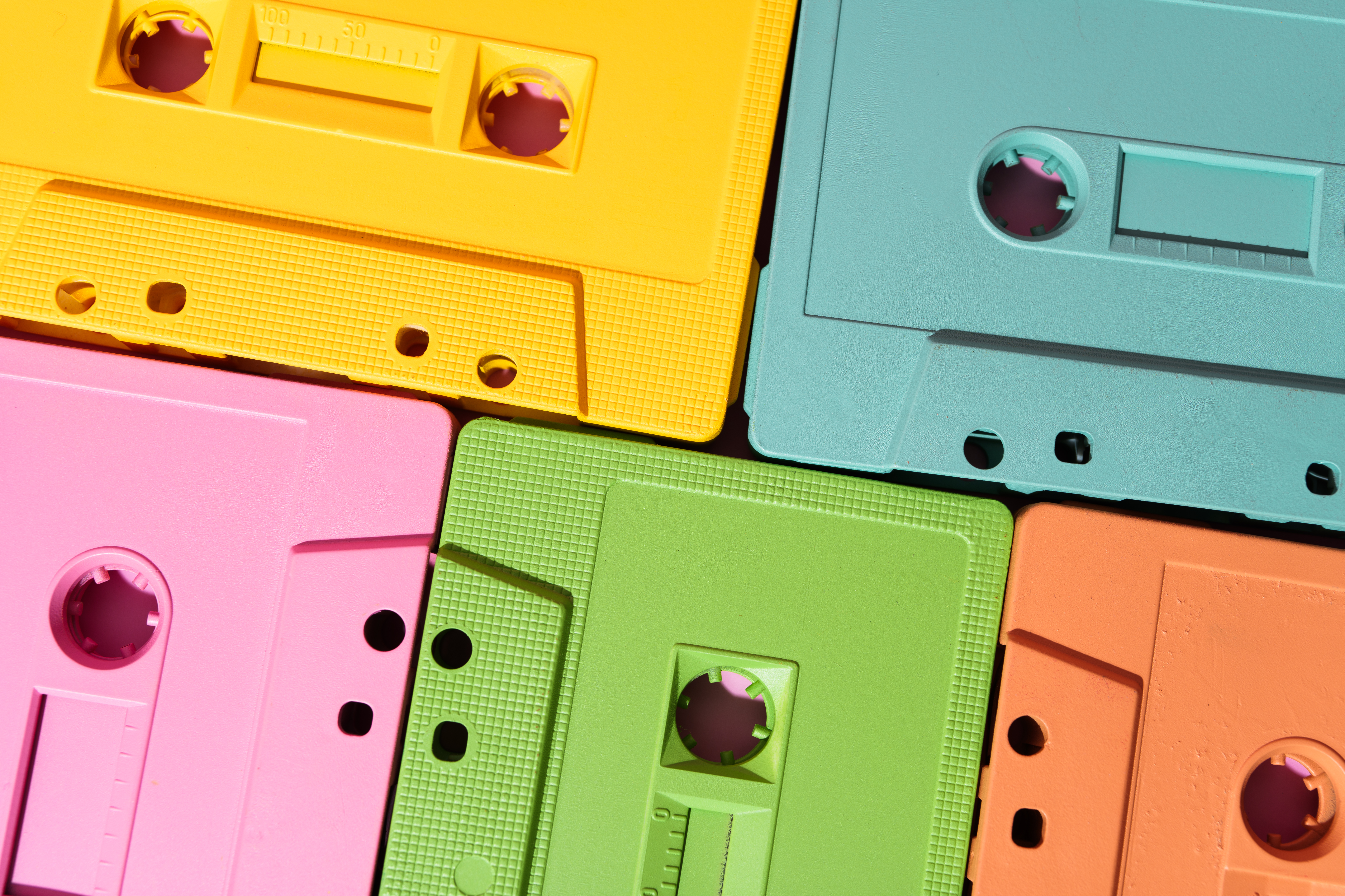 Vibrant cassette tapes in yellow, pink, green, blue, and orange, stacked together creating a nostalgic retro background