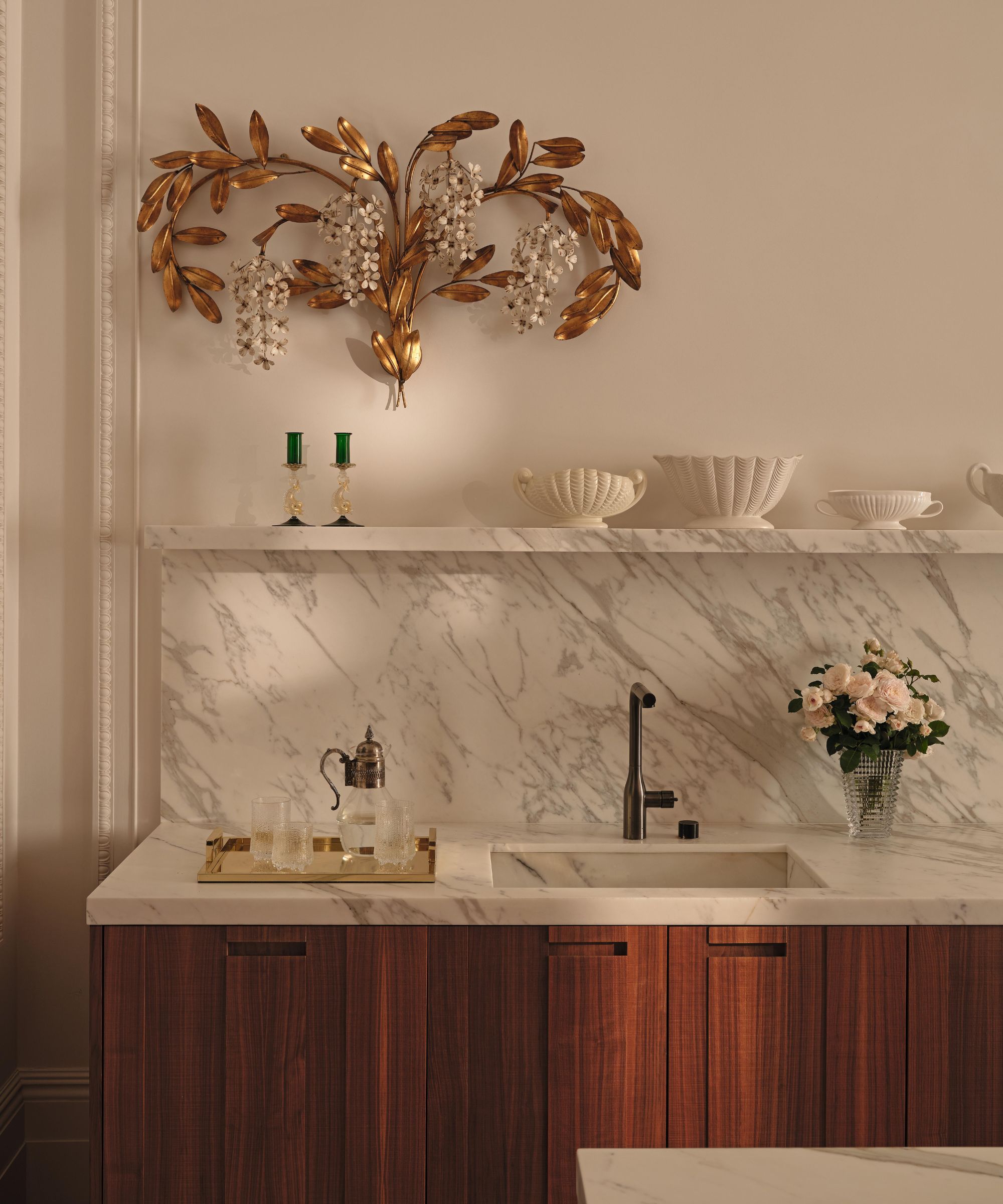 an elegant kitchen with dark walnut cabinetry, marble counter and backsplash with a large brass floral vintage sconce