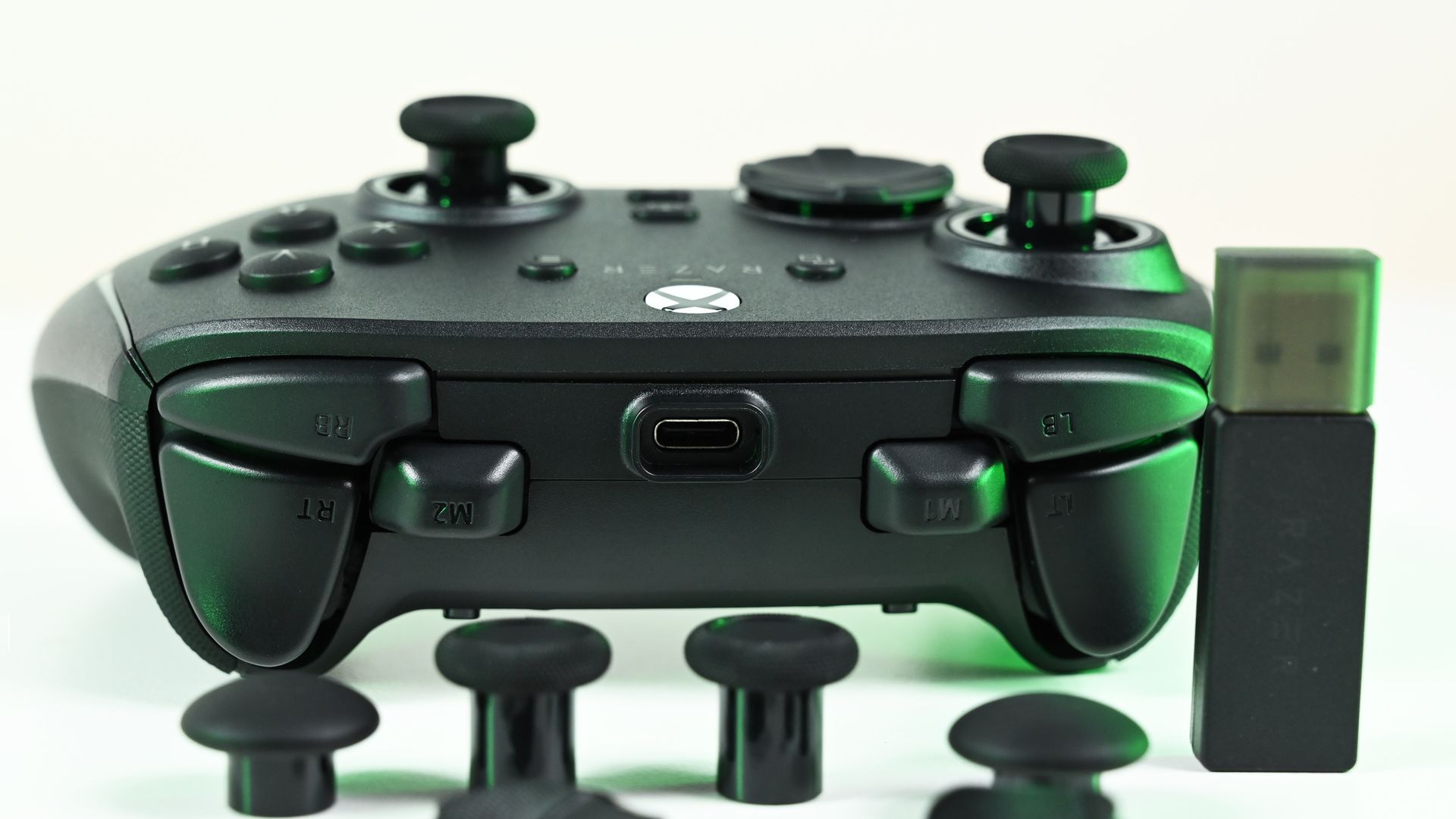 Top view of the controller's triggers, bumpers, and USB-C port, displayed with a USB wireless dongle and spare thumbstick caps.