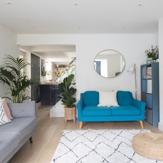 White living room with blue sofa, round mirror, berber rug, view to kitchen
