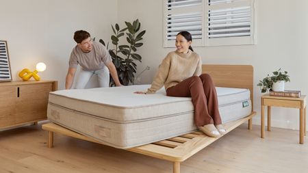 A woman sitting on the Eva Premium Adapt Mattress while a man adjusts it on a base